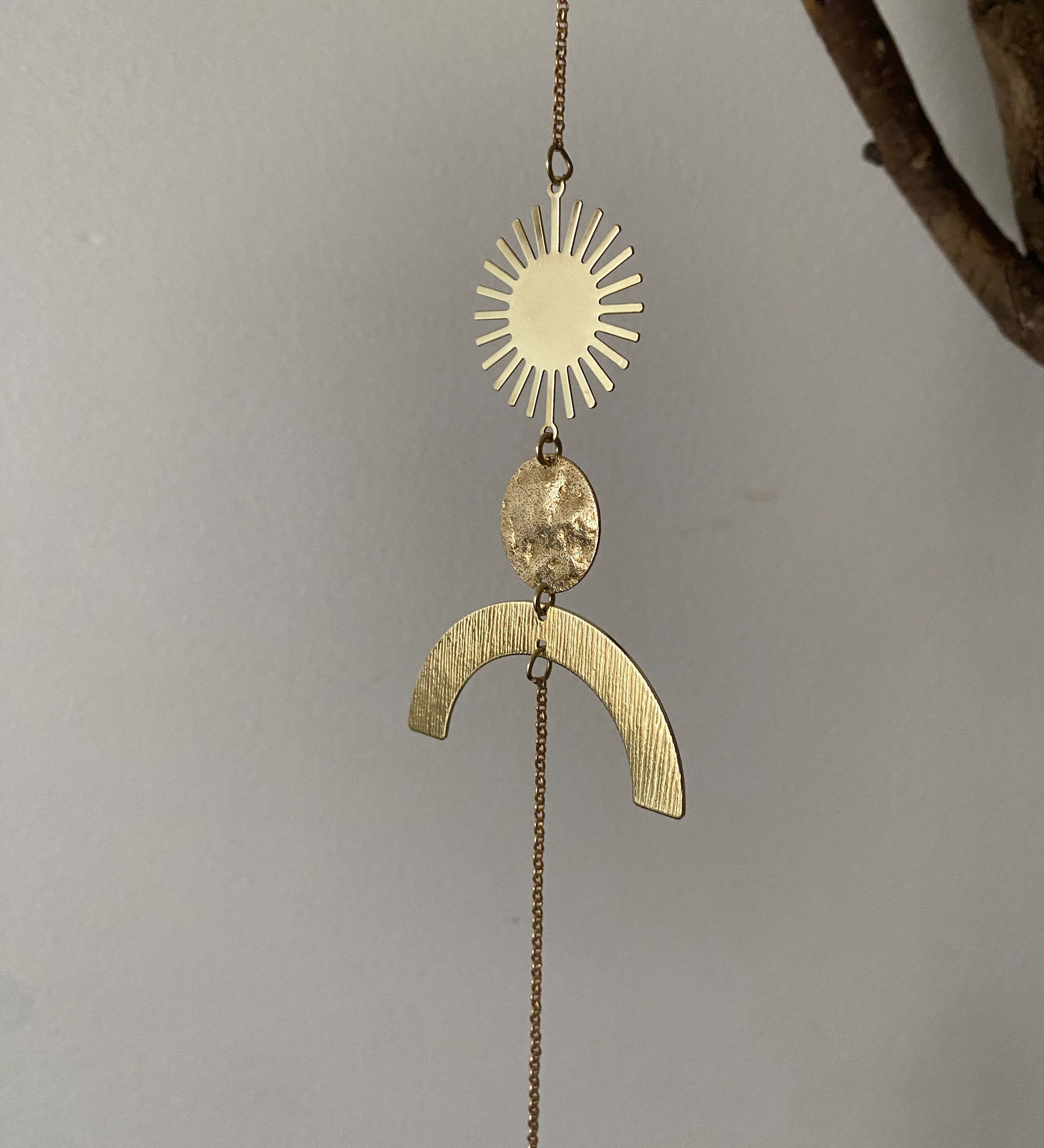 Gold pendant with sun and arch design on a chain against a gray background