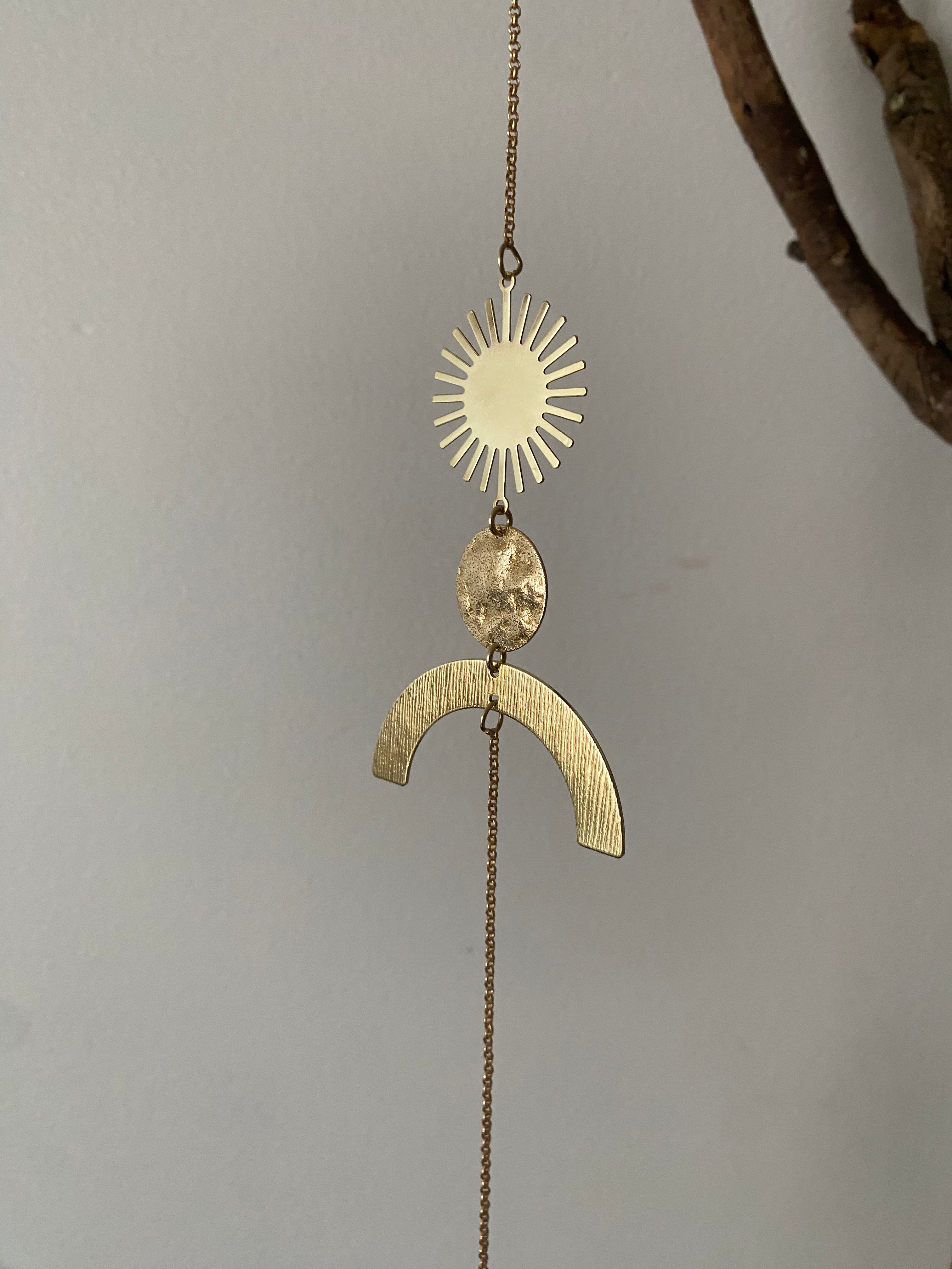 Gold pendant with sun and arch design on a chain against a gray background